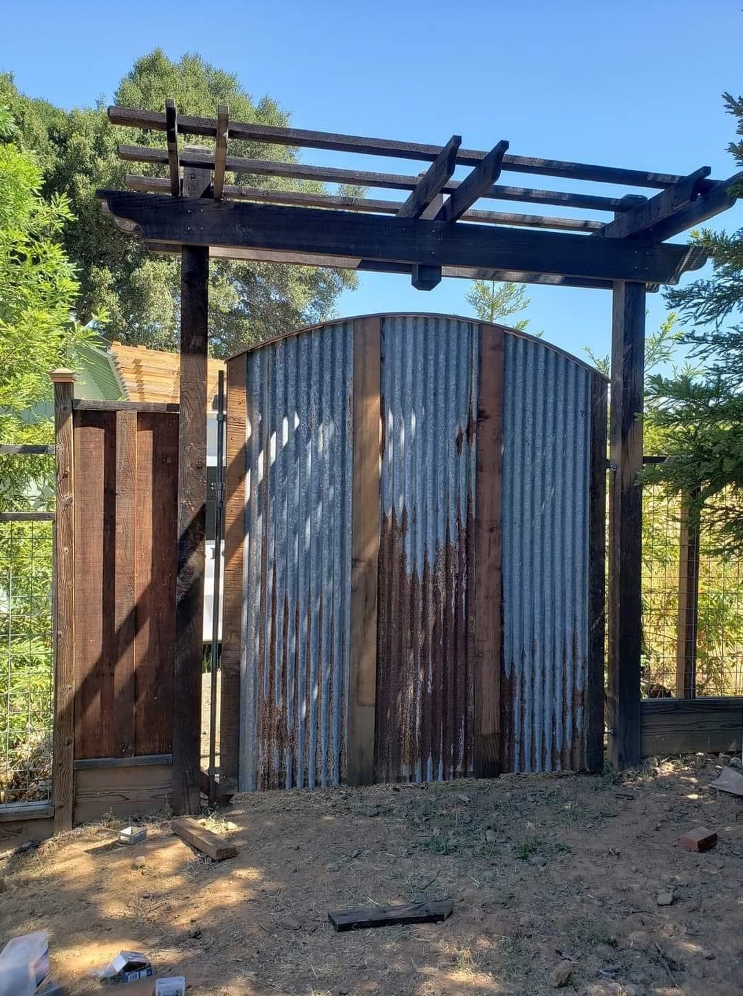 Custom arched gate of corrugated metal and redwood under a timber arbor, built by RLS Custom Carpentry in Mendocino County, CA